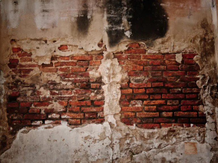 Backsteinmauer, von der der Putz abgefallen ist und die Ziegel freiliegen